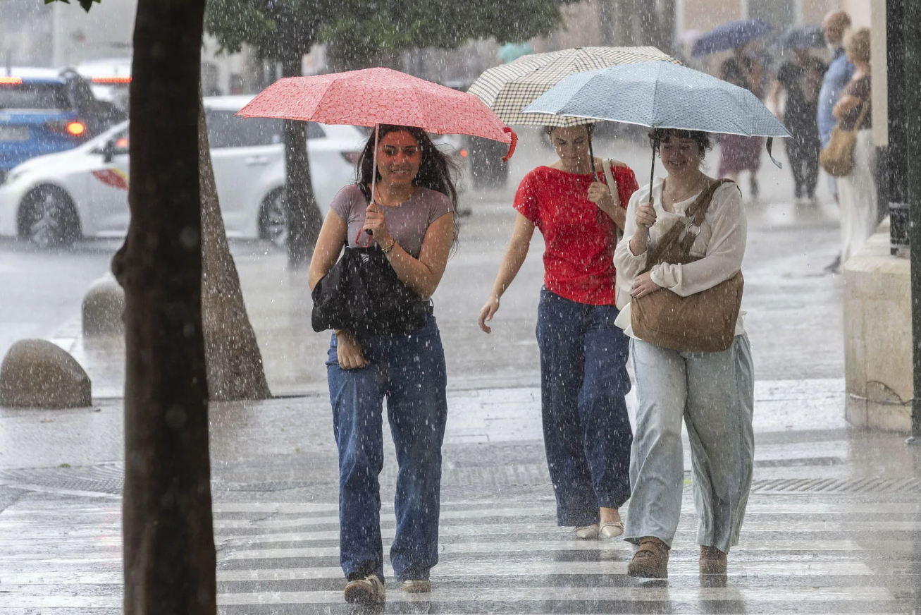 Varias jóvenes se resguardan bajo su paraguas de la intensa luvia que ha caido este viernes en la Plaza de la Cruz Roja de Murcia.