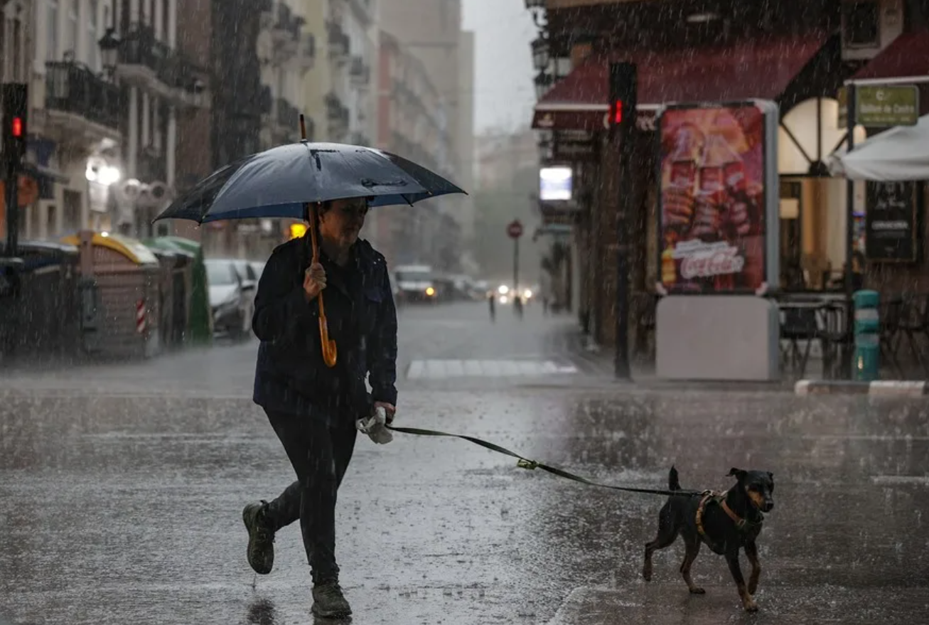 Una mujer pasea al perro bajo la lluvia en Valencia.